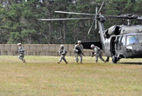 Four Army soldiers in training depart a landed Blackhawk helicoter with rifles in hand, onto an open field