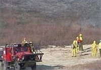 Fire professionals stand at the ready with trucks and brushbreakers watching from a high point overlooking the burn to watch smoke and make sure the fire does not go beyond the planned perimeters