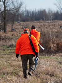 Two hunters dressed in orange gear walk through the woodlands during a day of deer hunting