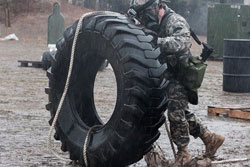 An Army soldier pushes a huge truck tire as tall as he is to a vehicle supply point.