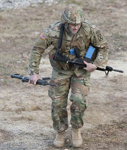 A soldier carrying a weapons runs across a dirt covered training area during a training exercise.