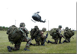 A group of soldiers kneeling on one knee keeping low waiting for an incoming helicopter to land during a training exercise.
