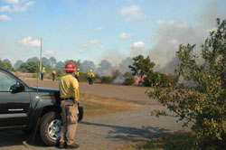 One of the workers in charge stands beside his truck from a distance watching over the low lying smoke of the controlled burn. 